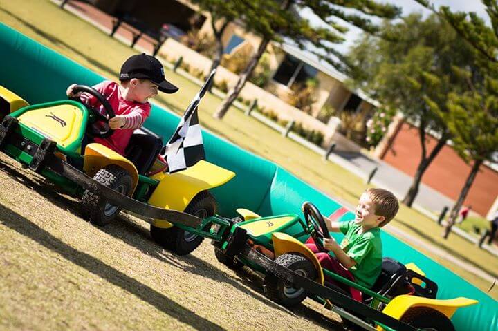 Some competitive, friendly kid racing - children seen on the go kart track designed for kids riding around having fun at an event in Perth