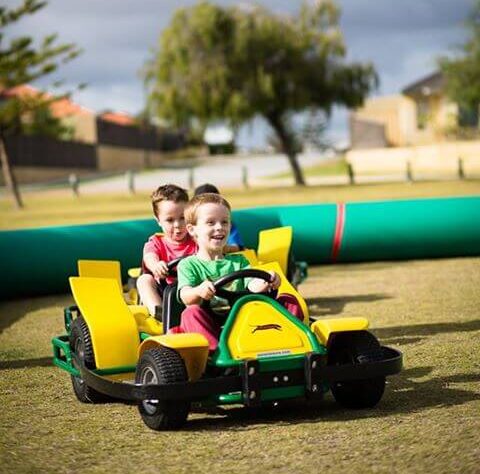 Two kids seen each on their go karts on the little go kart track at a party for kids
