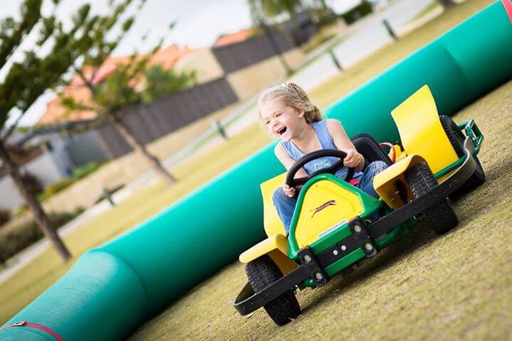 A child with a big smile as she races by on her go kart on the track